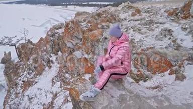 女人坐在山上。 旅行者正在山顶上散步。 漂亮的女孩穿着时尚的粉红色羽绒服