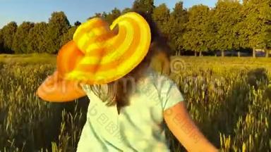 美丽的女孩戴着黄色的帽子在日落的天空上的绿色麦田上<strong>奔跑</strong>。 <strong>自由</strong>概念。 日落时的麦田。 慢慢
