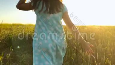 美丽的女孩戴着黄色的帽子在日落的天空上的绿色麦田上<strong>奔跑</strong>。 <strong>自由</strong>概念。 日落时的麦田。 慢慢