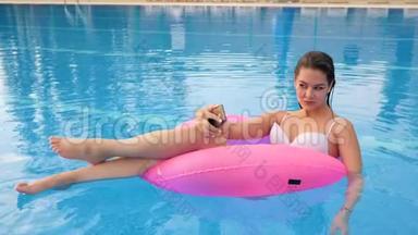 穿泳装的女孩在电话上拍照，在度假时在游泳池边游泳进入充气圈