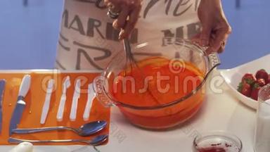 女人`她的手正在白色桌子上的大玻璃锅中搅动橙色的物质