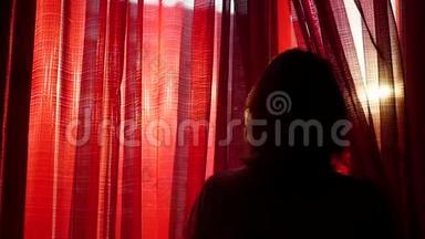 女孩打开红色的窗帘，用手在阳光`的光线下玩耍。 女孩的剪影