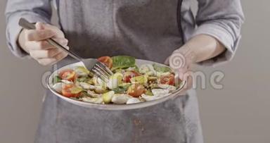 一个女人穿着围裙别针，带叉子鹌鹑蛋，在盘子里放着沙拉和鹌鹑蛋，还有鸡片