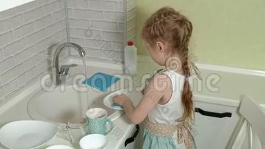 穿着<strong>围裙</strong>的漂亮小<strong>女孩</strong>站在椅子上，在明亮的厨房洗碗，帮助父母