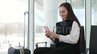 在机场候机楼等待航班时，一位开朗的女商人在智能手机上发短信，快乐的微笑女孩模特