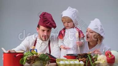 可爱的小男孩和他美丽的父母在厨房做饭时微笑。 年轻家庭在厨房做饭