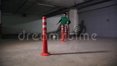 地下停车场。 运动足球男子训练他的足球技能。 带球穿过障碍物