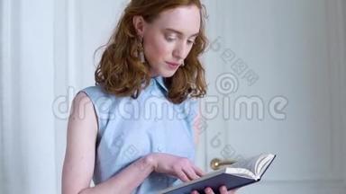 年轻的红头发女孩拿着一本书在白<strong>屋子</strong>里看书