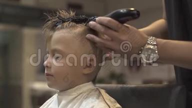 儿童理发店用电动剃须刀理发的小男孩画像。 使用电动剃须刀的发型师