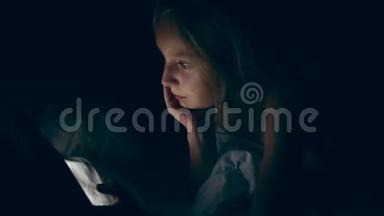 年轻的白种人白人女孩晚上躺在床上看视频。 小女孩看手机平板电脑的电影。