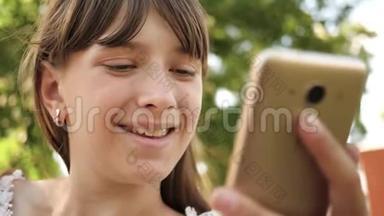 快乐女孩用智能手机在长凳上的公园里翻页。 特写镜头。 年轻的千禧年