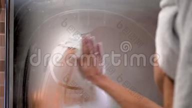 年轻的成年女人在雾蒙蒙的浴室里擦镜子玻璃，洗澡后看着朦胧的倒影。 空气中弥漫着浓浓的水汽