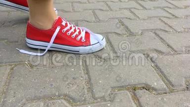 女人在红色运动鞋上系鞋带。 女人`穿着红色运动鞋在城市的道路上