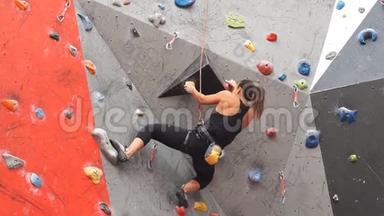 漂亮年轻的运动女孩爬在室内攀岩墙上。