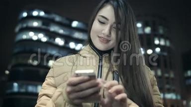 这个女孩正在夜间城市的背景下，在智能手机上写课文。