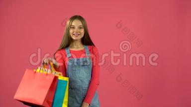 手里拿着袋子的购物狂女孩站着，开始微笑。 粉色背景