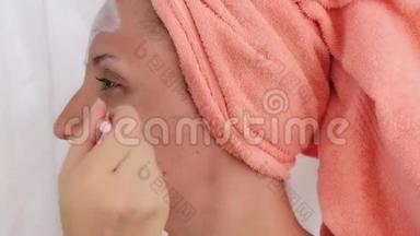 年轻女人用刷子在脸上涂化妆品面膜。 女孩，在她的脸颊上涂了一个面罩。 女孩做她的脸