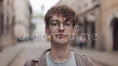 年轻的嬉皮士戴着眼镜站在城市街道上看镜头的肖像。 旅游、旅游