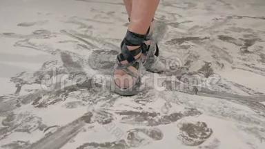 舞女的特写`芭蕾舞女的双腿在舞池里用黑色的尖鞋表演舞蹈，地板上撒满了白色的灰尘