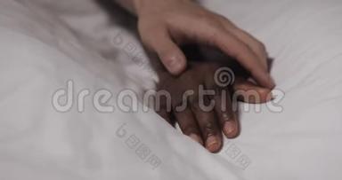 恋爱中的多民族夫妇躺在床上。 快关门。 女人的手躺在床上，男人的手在抚摸它