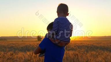 两个男孩在日落时在一片麦田里玩着金色的小穗。 一个男孩坐在另一个男孩的肩膀上