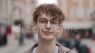 年轻的嬉皮士戴着眼镜站在城市街道上看镜头的肖像。 旅游、旅游