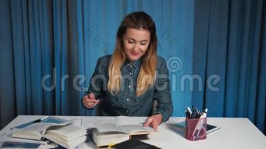 一个穿牛仔衬衫的快乐学生，读一本书，在工作簿上写作。