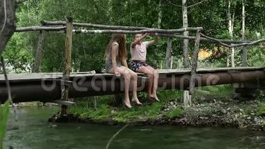 青少年坐在一座山河上一座狭窄的木桥上。 野营和冒险概念