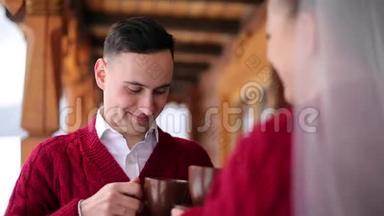 新郎和新娘在村里木木木屋的阳台上用杯子喝咖啡或茶，然后用雪吻