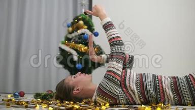 快乐的节日女孩躺在地板上的金色<strong>闪</strong>光纸屑和自拍发<strong>送</strong>吻。 装饰圣诞树