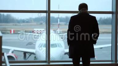 老人站在全高，凝视机场候机楼窗外，侧影观景.. 在机场看飞机。