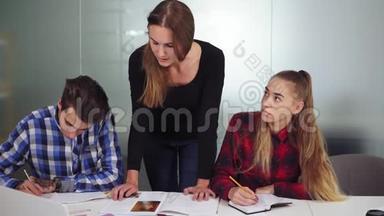 三个正在做作业的学生坐在桌子旁，一个女孩在听写，另外两个在做作业