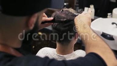 一位坐在镜子旁的客户的后景，当时一位留胡子的理发师正在用剪刀<strong>剪头发</strong>，他正在梳头