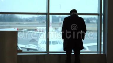 老人站在全高的位置，凝视机场候机楼的窗外，侧影观景.. 在机场看飞机。