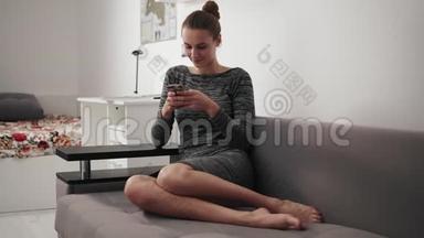 圆形镜头移动：微笑的年轻女子坐在家里的沙发上看着电话，打字留言