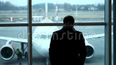 老人站在全高的位置，凝视机场候机楼的窗外，侧影观景.. 在机场看飞机。