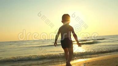 一个小男孩在沙滩上跳着跳着跑，然后以缓慢的速度在水中溅起水花。