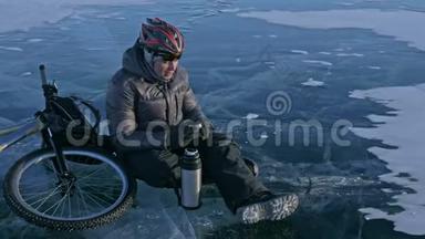 那个人正坐在冰上自行车的轮子上休息。 他<strong>喝热水</strong>瓶里的茶。 骑自行车的人穿着