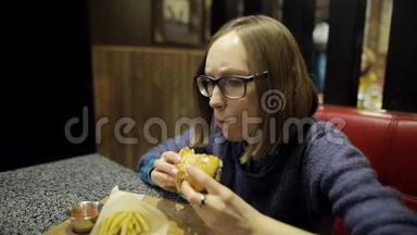 小女孩正在咖啡馆里吃美味的汉堡和薯条。 戴眼镜的女人对她的品味感到失望