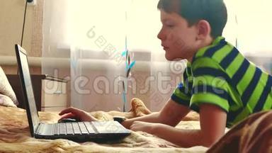 小男孩在卧室里用笔记本玩床。 室内笔记本电脑上的青少年社交媒体互联网