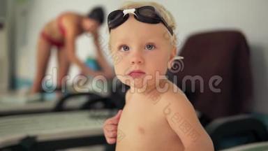 一个戴着护目镜的漂亮孩子坐在泳池边，看着镜头等待母亲的画像