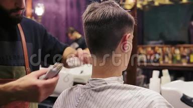 回头看一个客户被理发师剪了头发。 留胡子的理发师正在用电动理发器理发