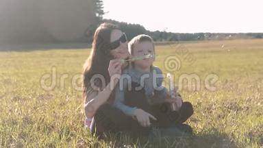 妈妈和儿子坐在草地上吹肥皂泡，<strong>全家</strong>周末在公园。