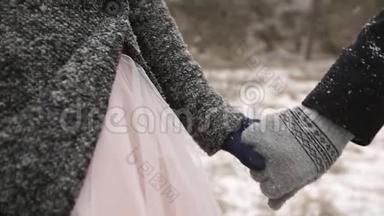 特写新郎牵着新娘的手在冬天下雪时在松林散步的视频。 下雪
