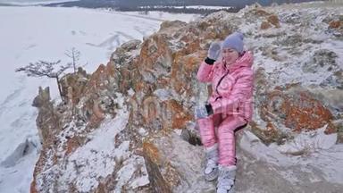 女人坐在山上。 旅行者正在山顶上散步。 漂亮的女孩穿着时尚的粉红色羽绒服
