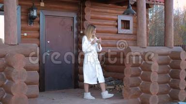 穿着白色浴衣和拖鞋的女人，带着咖啡走进<strong>门廊</strong>和木屋
