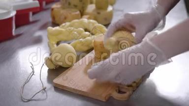 奶酪制造商正在一张桌子上的木制砧板上切割最终的奶酪产品，并特写了手