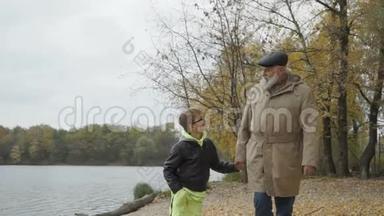 祖父和小孙子在河边的秋天公园散步