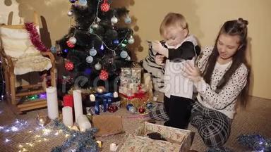 那个小男孩和他妹妹在装饰精美的圣诞树旁打开`新年礼物盒。 孩子是