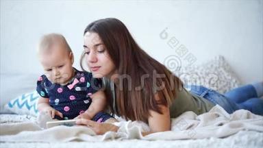 漂亮的女人和她可爱的宝宝躺在床上，用手机看动画片